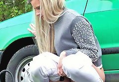 Bright blondie in white pants sits near the green car and pisses