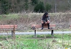 Raven haired petite babe sits on bench and pisses